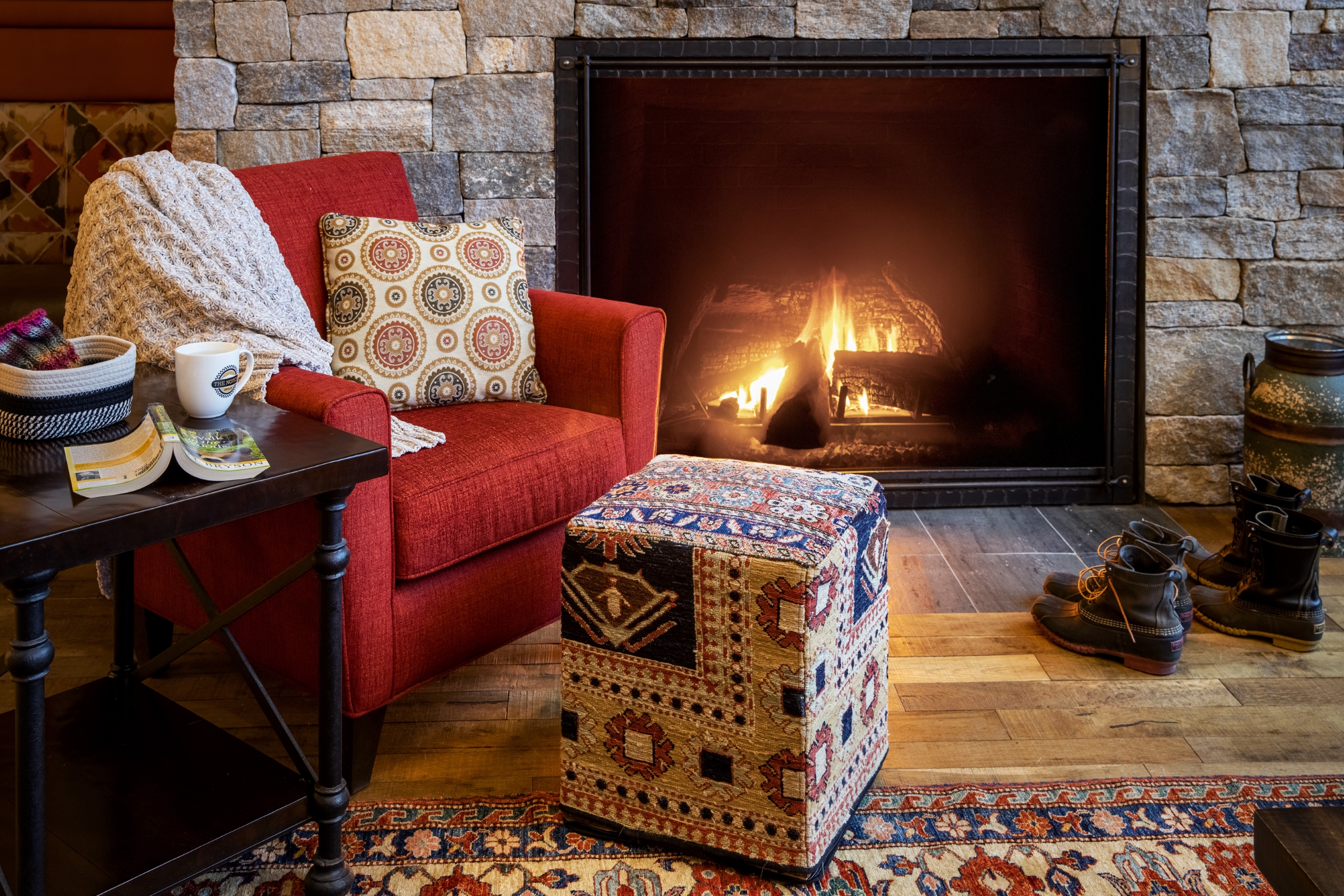 A comfy chair with an ottoman in front of a stone fireplace